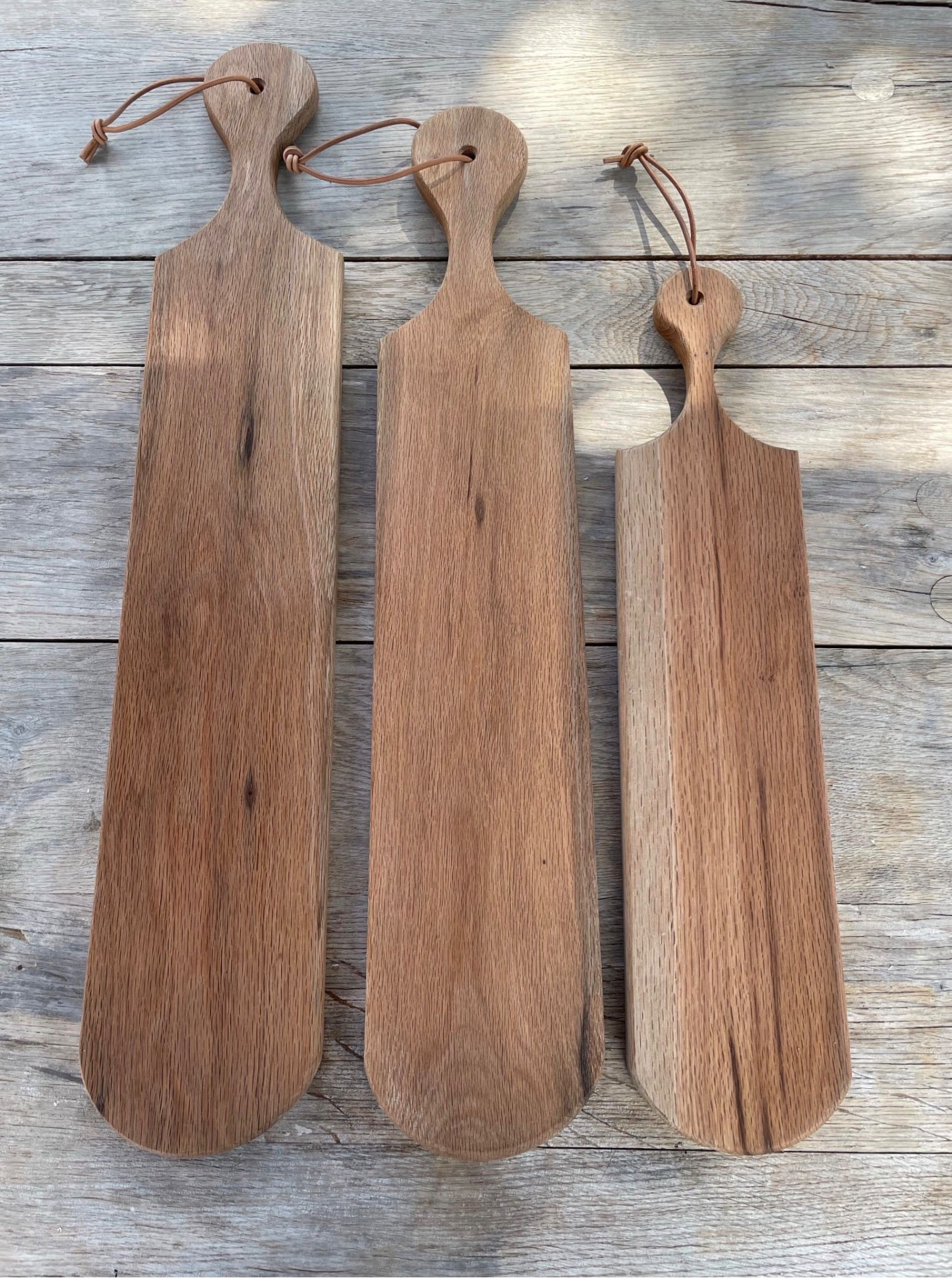 Three handcrafted wooden serving boards with leather hanging straps on a rustic wooden surface